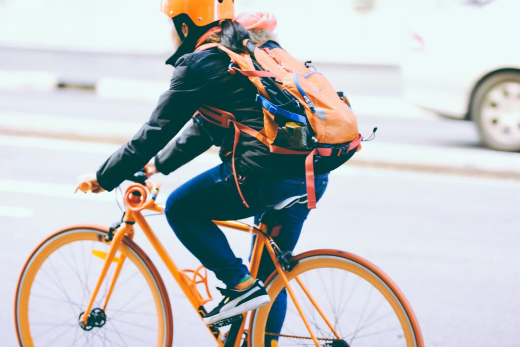Człowiek w bezpiecznym kasku i na pomarańczowym rowerze - hulajnoga elektryczna zamiast roweru