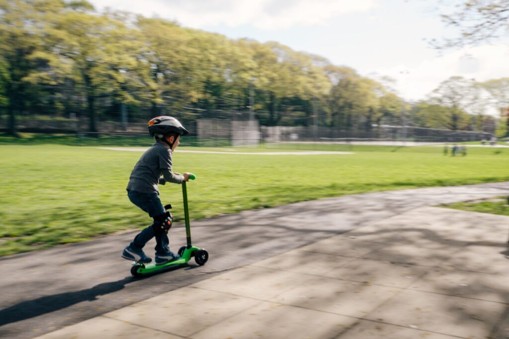 Dziecko jadące na hulajnodze po ścieżce pośród trawy - hulajnoga elektryczna zamiast roweru